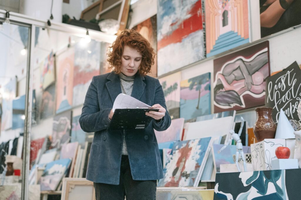 pexels-photo-6816594-6816594 A woman artist reviews her work in a vibrant art studio filled with colorful paintings and creative supplies.